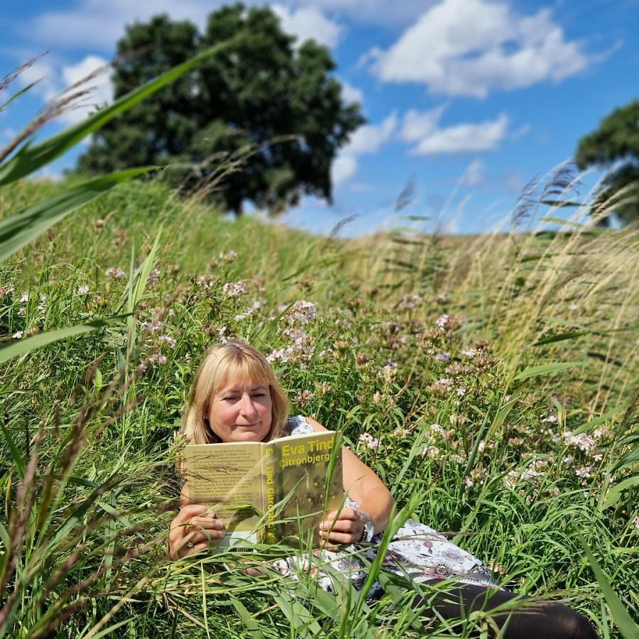 Foto af Lotte der læser 'Citronbjerget' på en eng med højt græs